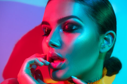 Fashion model woman in colorful bright lights with trendy makeup and manicure posing in studio