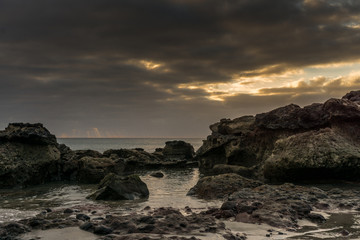 Fototapeta na wymiar Sunset on the beach of Fuerteventura with lava rocks, dark clouds and small waves