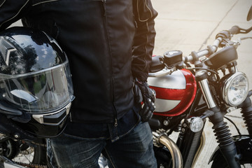 Fototapeta premium Biker nosić garnitur kurtki trzymać kask z motocyklem retro