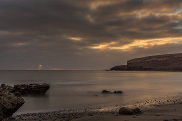 Sunset on the beach of Fuerteventura with lava rocks, dark clouds and small waves as long exposure