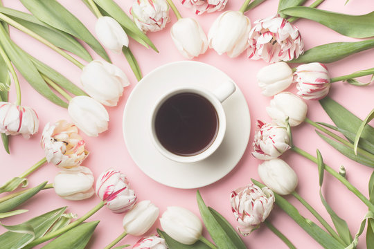 Spring morning concept. Flat-lay of a cup of coffee and flowers over light pink background, top view