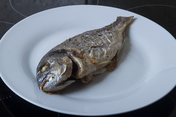 cooked sea bass on the grill lies on a white plate on a black