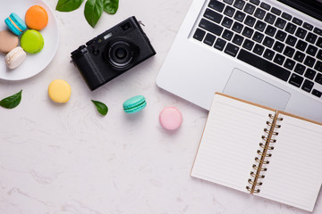 White desk with colorful macaroons, camera and laptop
