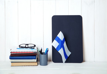 Books, notebooks, textbooks, glasses, a flag of Finland on a wooden table. Education in Finland.