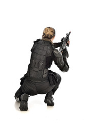 Fototapeta premium full length portrait of female soldier wearing black tactical armour, seated pose holding a gun, isolated on white studio background.