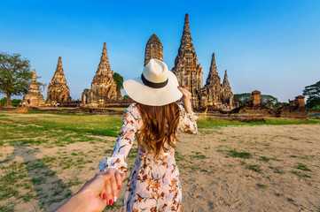Woman holding man's hand and leading him to Ayutthaya Historical Park, Wat Chaiwatthanaram Buddhist temple in Thailand.
