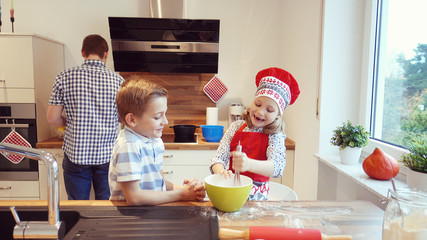 Young father with two happy children backing cookies in modern kitchen