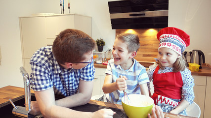 Young father with two happy children backing cookies in modern kitchen