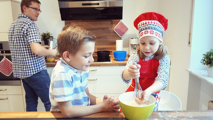 Young father with two happy children backing cookies in modern kitchen
