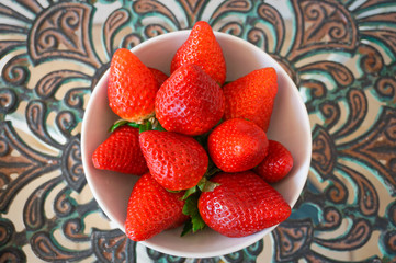 Big red strawberries in white bowl on metal table