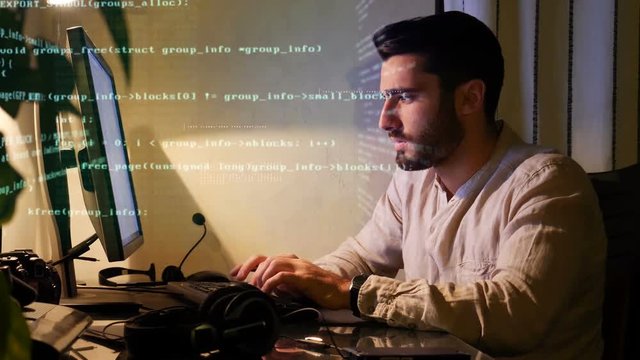 Young handsome male programmer coding at night, working at his computer at home, with code appearing over image