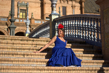 a beautiful girl dressed in flamenco happy and smiling sitting on the steps