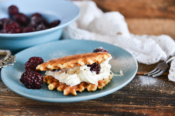 Round waffles with fresh blackberries and whipped cream, on natural wooden background in rustic style