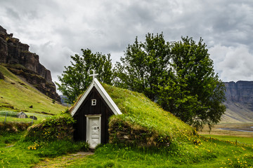 Fototapeta premium Icelandic traditional turf church covered with grass, trees and rocks in the background near Kalfafell village, South Iceland