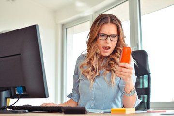 Furious businesswoman wearing suit working on line using a smart phone in a desk at office