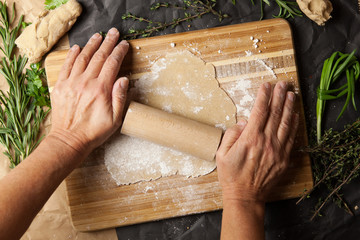 Woman's hand rolling dough on wooden cutting board. Top view.