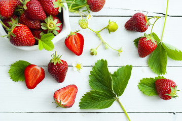 fresh ripe and under ripe strawberry fruits, flowers, leaves on white wood table background