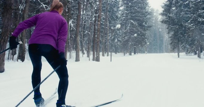 TRACKING Young adult Caucasian female athlete practicing cross-country skiing on a scenic forest trail. 4K UHD 60 FPS SLO MO