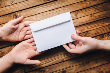 Hand pass the white envelope to the other hands on a wooden background. Transfer of money for donation. To send a letter.