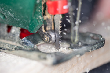 a green jigsaw saws a bright plank