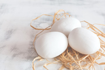 Three white Easter eggs lying on a hay on a white wooden vintage background.