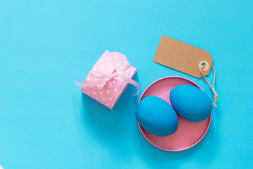 The blue Easter egg lies in a brightly pink metal box. Near the pink dots box and an empty label in place with your text. Blue background. Copy space.