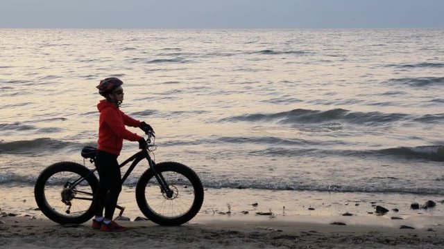 Fat bike also called fatbike or fat-tire bike in summer driving on the beach. Beautiful girl and her bicycle in the beach sand. The girl is out of focus. Focus on the sea.