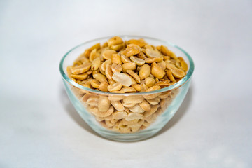 Peeled roasted peanuts with salt in a large glass bowl on a white background
