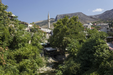 Mostar in summer season, with green trees and the sffluent of Neretva river, with minaret in the...
