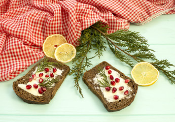 Black bread with grenades berries on turquoise wooden background. Christmas food, Christmas decorations with lemon, juniper, branch, red berries