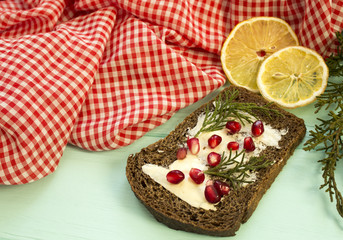 Black bread with grenades berries on turquoise wooden background. Christmas food, Christmas decorations with lemon, juniper, branch, red berries