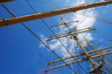 Steel masts of a sailing ship with the lowered sails with blue sky on the background.