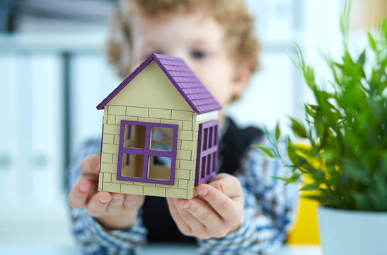 Hands of the boy holding the plastic figure of house. Real estate and family home security concept.