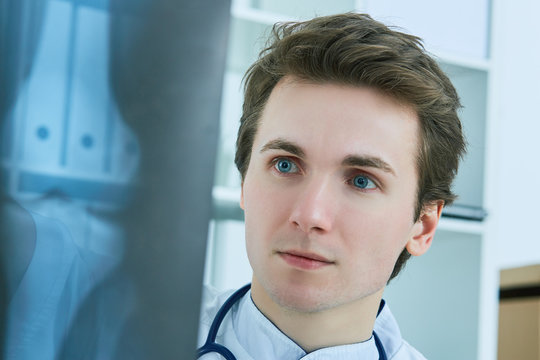Close up portrait of young male doctor holding x-ray or roentgen image.