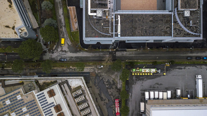 Perpendicular aerial view of a road in an industrial areaof a big city. Nobody is on the street. There are only a few cars, trucks and vans parked on the asphalt. The building is an office.