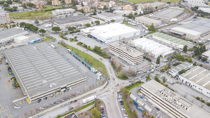 Aerial view of an industrial area of a large Italian city with warehouses, warehouses, offices and buildings. Among the asphalt roads beyond the cars, vans and trucks there are trees.