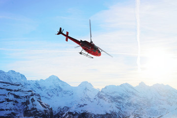 Red helicopter flying at Swiss Alps mountain Mannlichen winter sunset