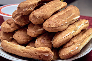 On the plate there are several home-made eclairs. Eclairs cut in half. Stuffed with vanilla butter cream. Handmade cakes. Sweets for a birthday or a holiday. Cakes are stacked in a pile.