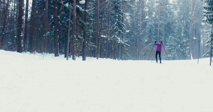 Young adult Caucasian female athlete practicing cross-country skiing on a scenic forest trail. 4K UHD 60 FPS SLO MO