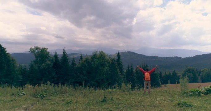 Man standing on edge at mountain peak while raising hands