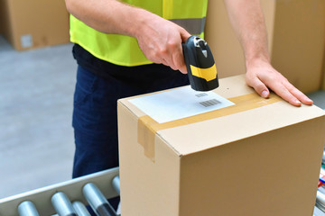 Versand im Onlinehandel - Logistik - Arbeiter scannt Barcode von Paket mit Waren // Shipping in e-commerce - Logistics - Workers scans barcode of parcel with goods