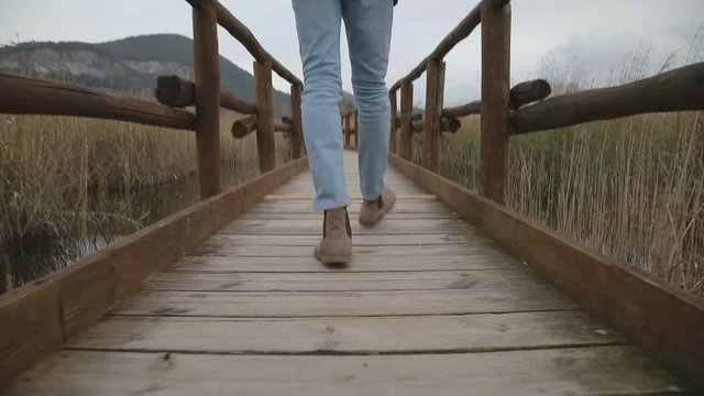 Ragazzo sta camminando su un piccolo ponte di legno in una palude mentre riprende con la sua telecamera
