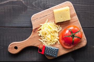 Cutting board with and grater cheese on wooden background. Top view.