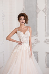 Morning of the bride. A beautiful bride stands in a wedding dress. Wedding hairstyle and makeup. Hand at waist.  Dress with lace.