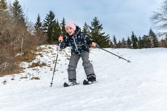 Winter snow activity. Front view of a girl skiing downhill surrounded by trees.