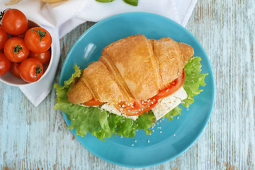 Plate with delicious croissant sandwich on wooden table