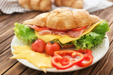 Plate with delicious croissant sandwich on wooden table