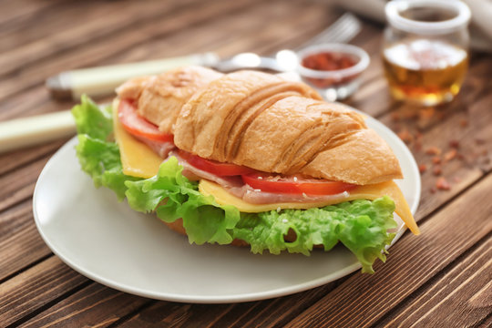 Plate with delicious croissant sandwich on wooden table