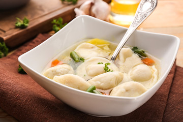 Bowl with tasty broth and dumplings on table