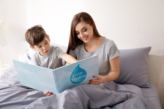 Mother and her son reading book on bed in children room